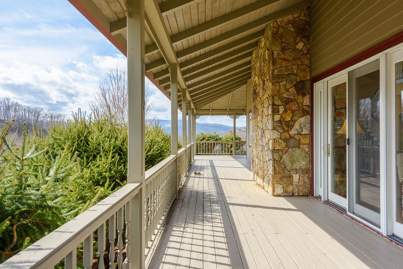 A covered porch with a stone wall, wooden railing, and large glass doors.