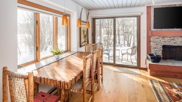 Un coin repas chaleureux avec une table et des chaises en bois, de grandes fenêtres et une cheminée en pierre.