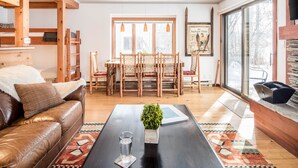 Un salon chaleureux avec un canapé en cuir, une table à manger en bois et des chaises. On peut voir un verre d’eau sur la table et une petite plante.