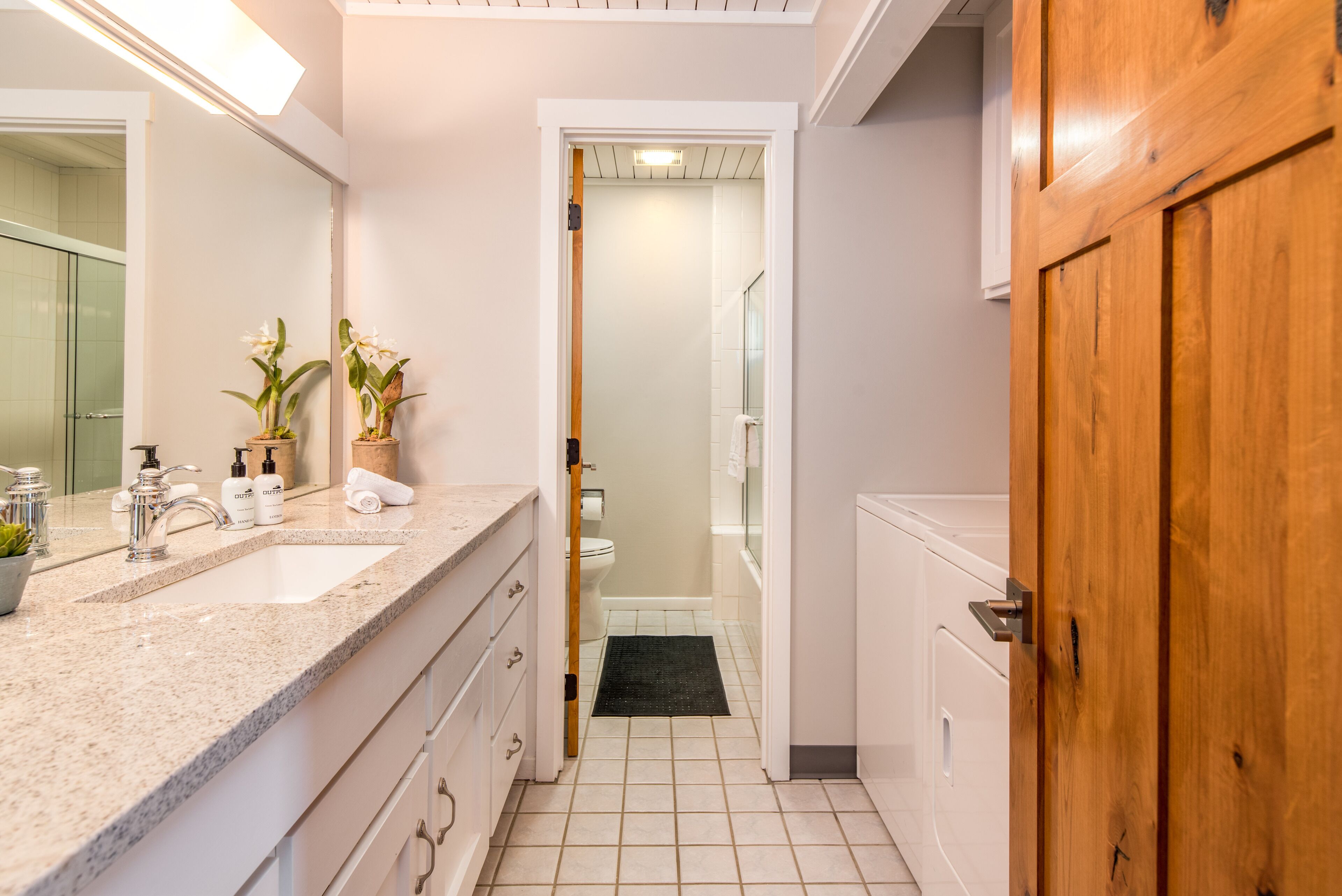 Un baño con lavamanos doble, un espejo, una planta en maceta y una puerta de madera.