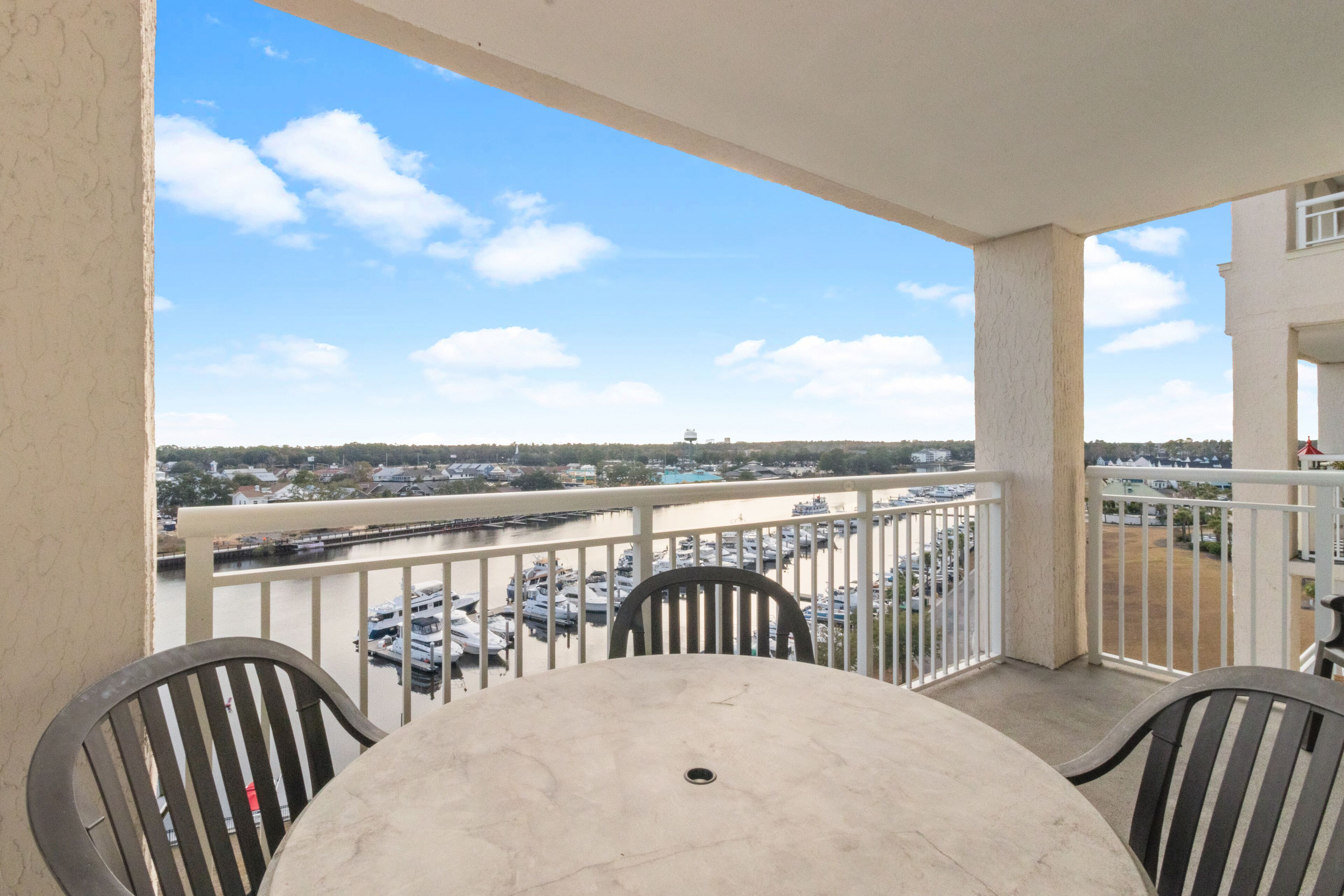 A balcony with a table and chairs, overlooking a marina with boats and a distant cityscape.