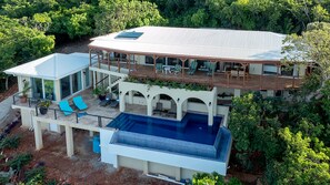 A modern two-story house with a large deck, a swimming pool, and a covered patio area.