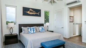 A bedroom with a bed, bedside tables, a bench, a painting, and a view of the outdoors.