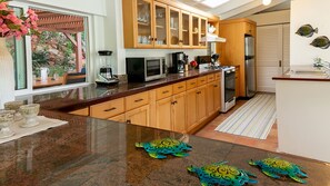 A kitchen with wooden cabinets, a granite countertop, a refrigerator, and a window with a view of greenery.