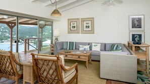 A spacious living area with a view of the sea, a wooden coffee table, a sofa with patterned cushions, and a wicker chair.