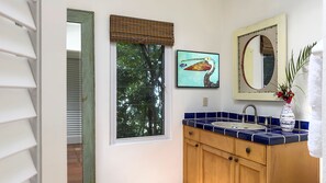 Een badkamer met een raam, een wastafel, een spiegel en een lijst met een schilderij.