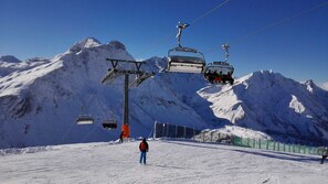 A ski lift system with chairs moving up and down the cable, a person skiing on the slope, and snow-covered mountains in the background. - Top 6 - House Annette (Schröcken)