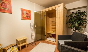 Een knus vertrek met een houten sauna, een rieten zitting, een klein houten tafeltje en een potplant.