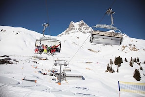 A ski lift with passengers, a chairlift, and a snowy mountain backdrop. - Top 6 - House Annette (Schröcken)