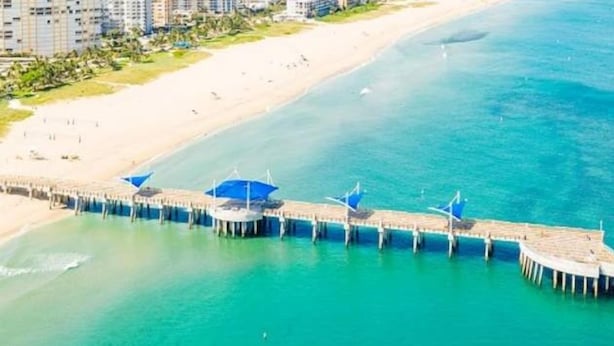 A coastal pier with a series of blue umbrellas, extending into the turquoise sea. - Blue Pearl for 10-Heated Pool-Beach-Pier 5 minutes (Pompano Beach)