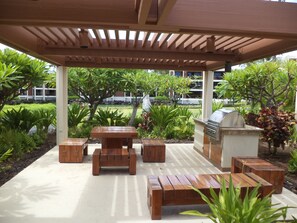 An outdoor patio with wooden furniture, a grill, and lush greenery.