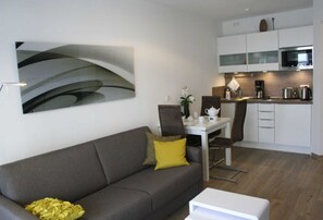 Una sala de estar moderna con un sofá gris, una mesa de centro blanca y una zona de comedor con mesa y sillas blancas.