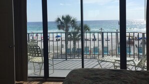 Ein Schlafzimmer mit großem Fenster mit Blick auf einen Strand, einem Deckenventilator und einem Bett mit floralem Bettbezug.