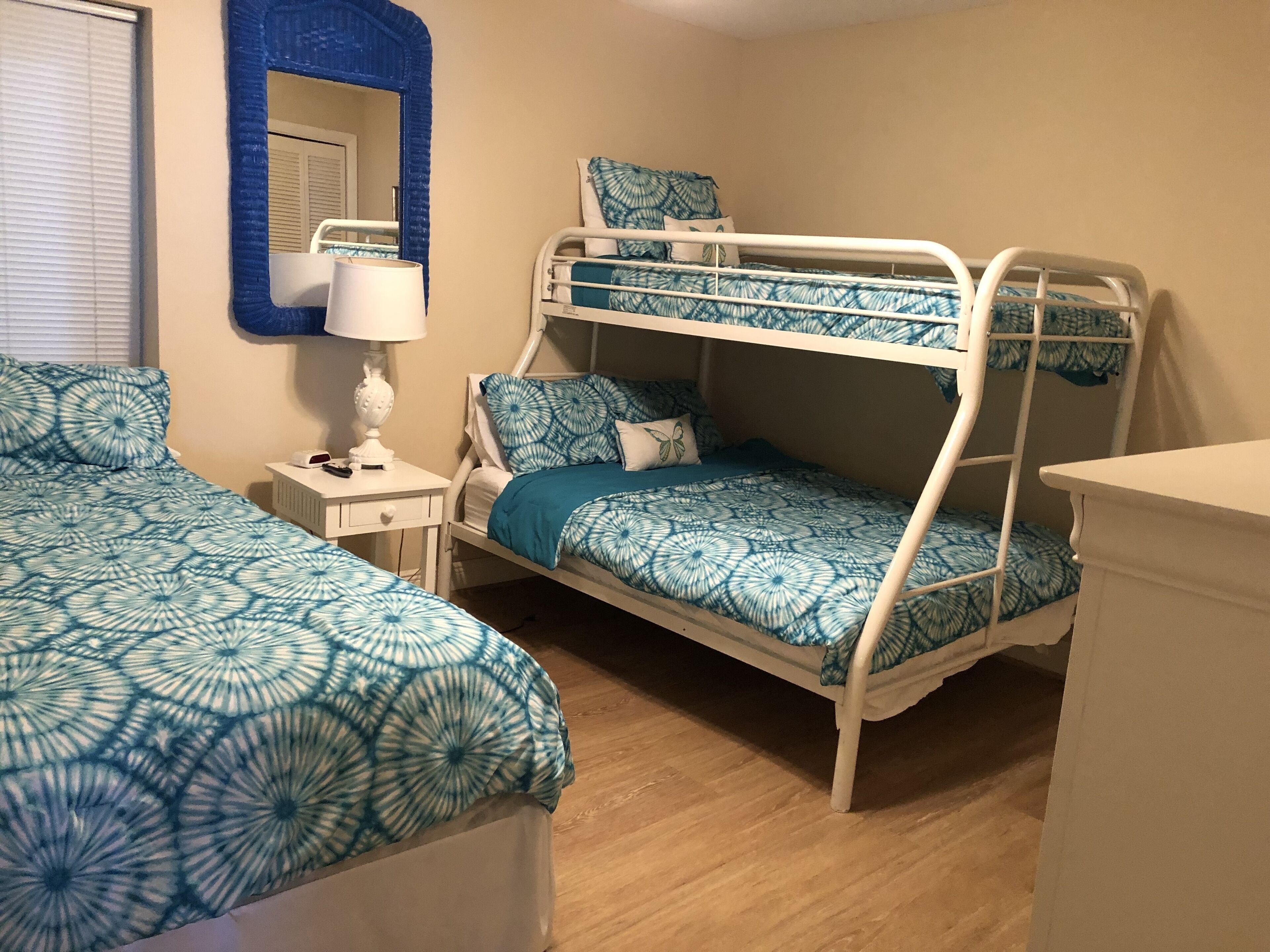 Habitación con literas a juego, ropa de cama azul, una mesita de noche con lámpara y un espejo en la pared.