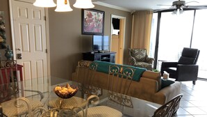 Ein Essbereich mit Glastisch und Stühlen, einer Couch, einem Fernseher und einem Deckenventilator.