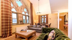 Una sala de estar acogedora con un sofá verde, un reposapiés escocés y un comedor con una mesa y sillas.