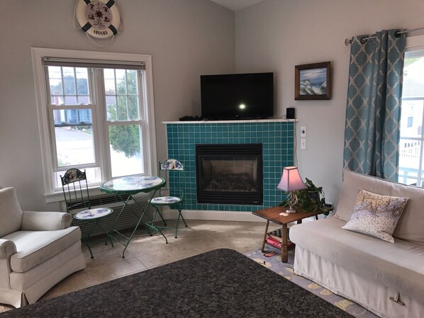 A living room with a fireplace, a television, a sofa, a dining table, and a chair.