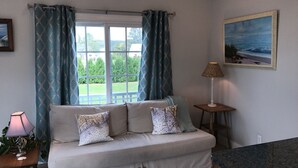 Ein Wohnzimmer mit einer Couch, einer Lampe, einem Gemälde und Blick ins Freie.