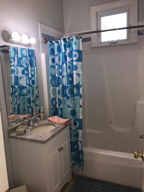 A bathroom with a vanity, sink, mirror, and a bathtub.