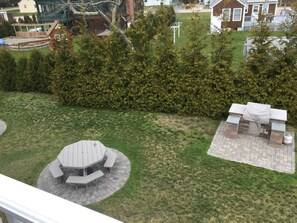 A backyard with a wooden table and benches, a brick barbecue area, and a well-maintained hedge.
