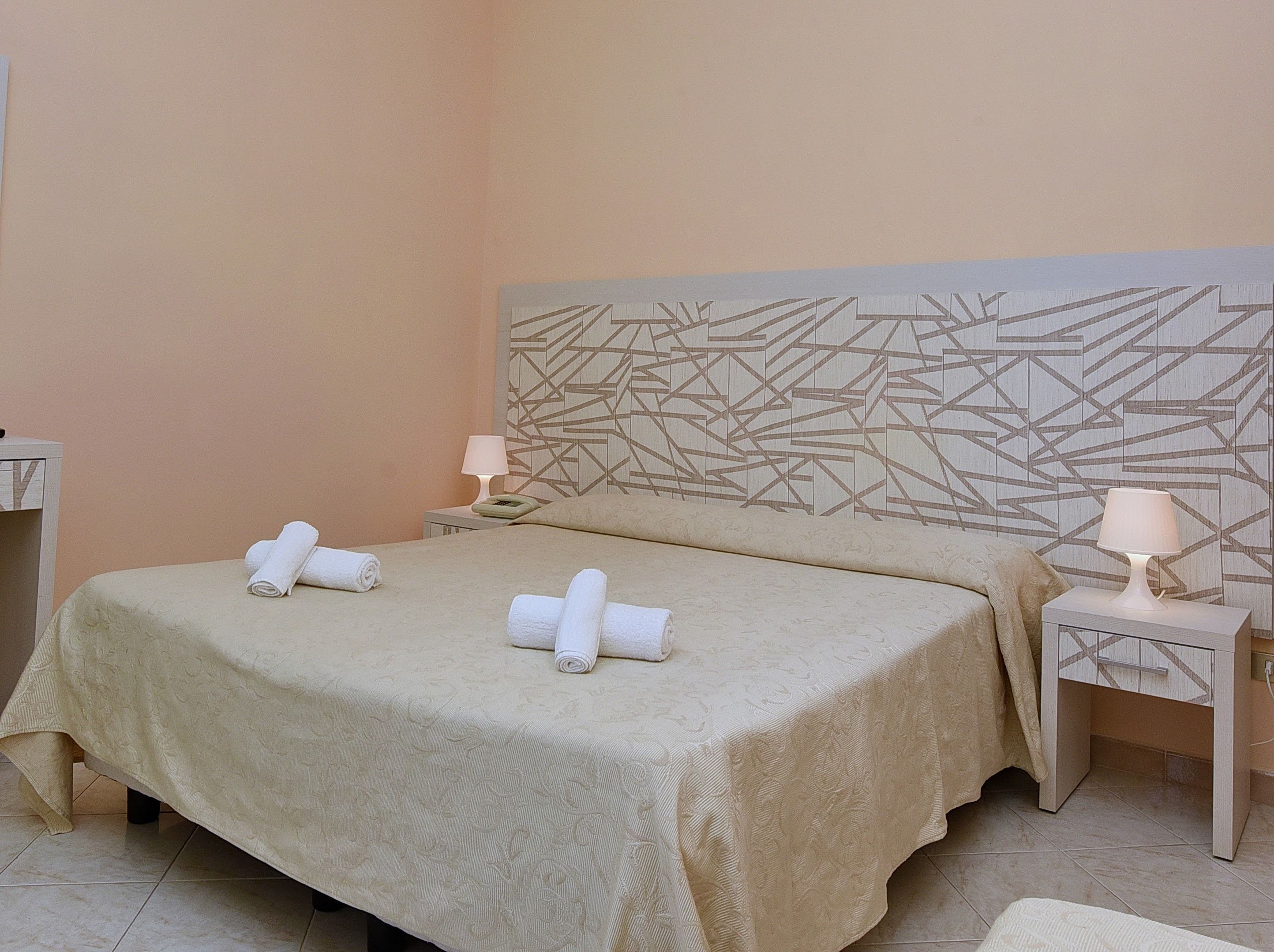 Una camera d'albergo con un letto, due comodini e una testiera con motivo geometrico.