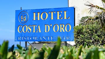 Ein blaues Schild mit goldener Schrift für das Hotel Costa d'Oro, das ein Restaurant/eine Bar anzeigt.
