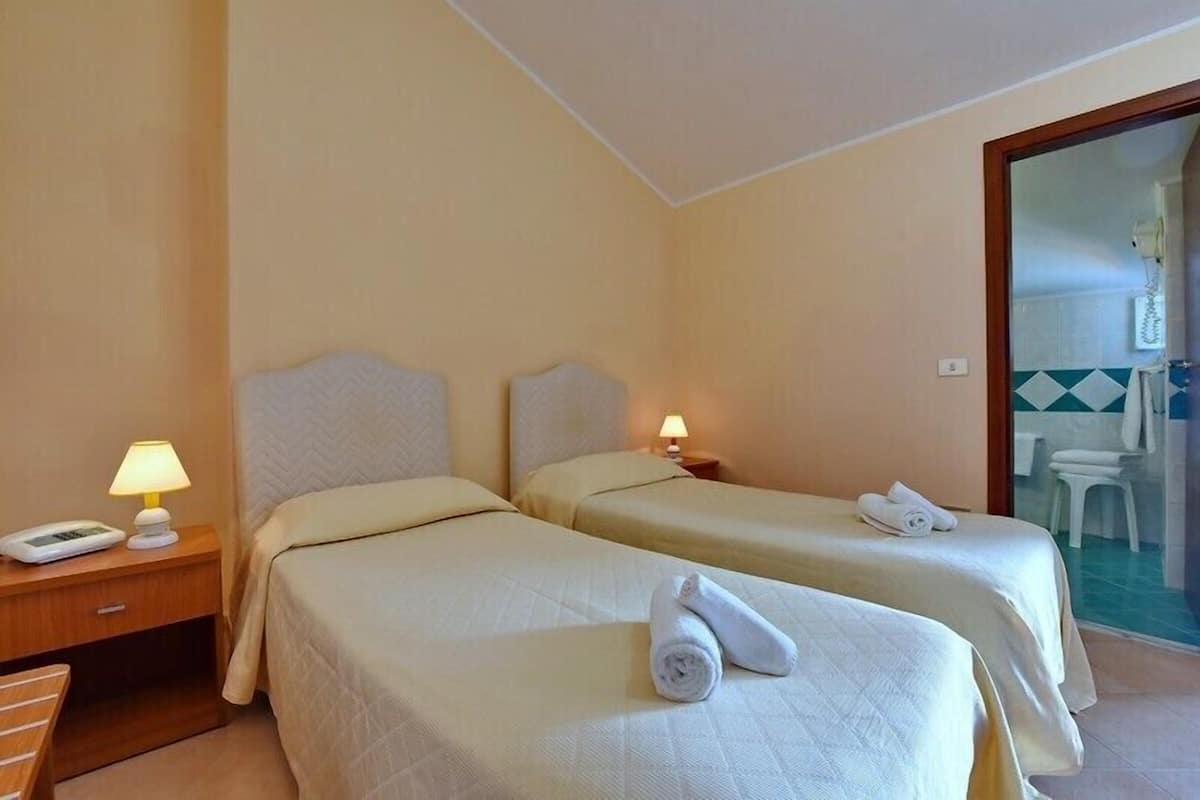 A hotel room with two beds, bedside lamps, a telephone, and a towel on the beds.