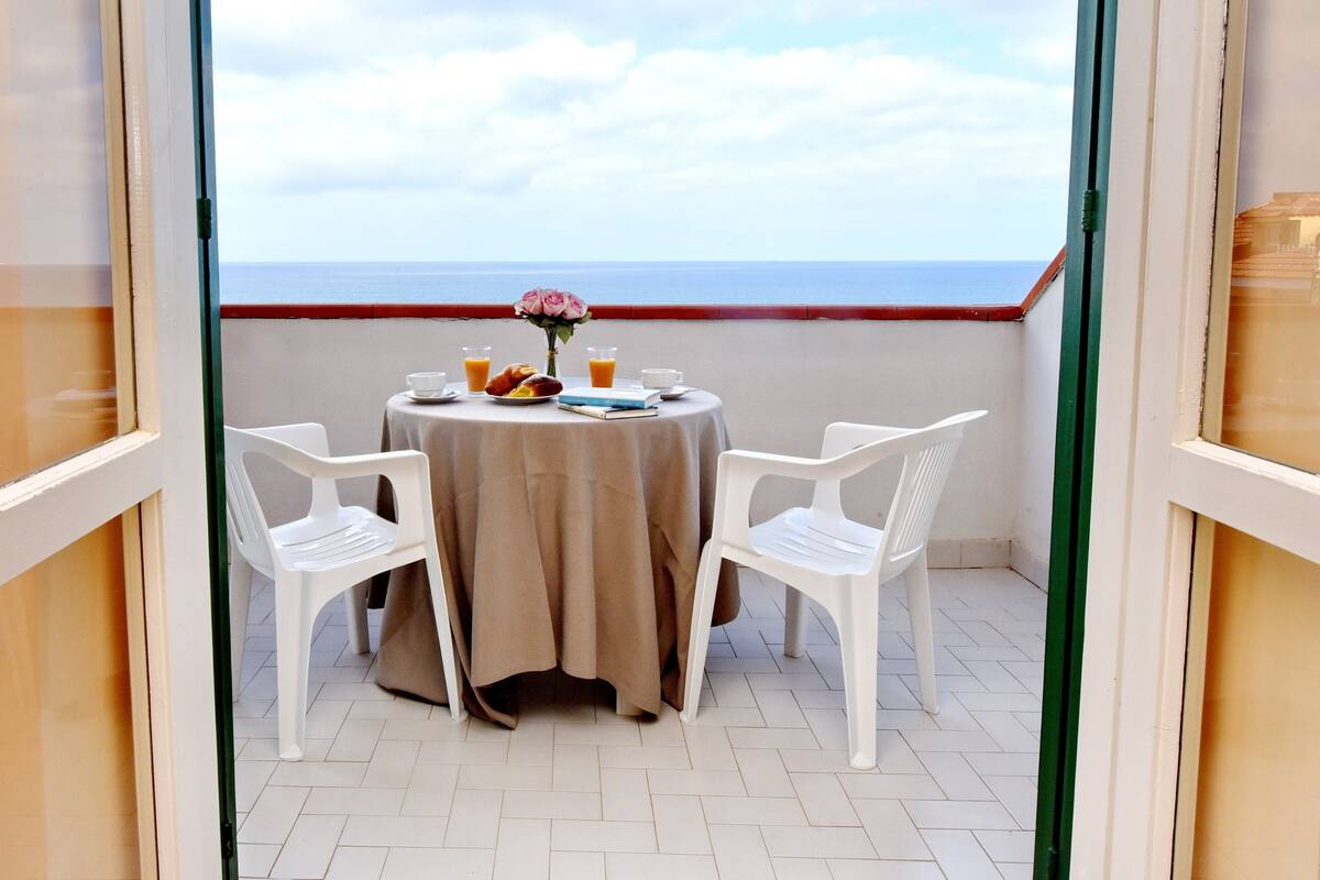 A balcony with a table set for breakfast, overlooking the sea.