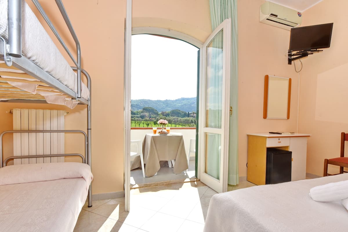 A hotel room with two beds, a desk, a TV, and a balcony with a table and chairs.