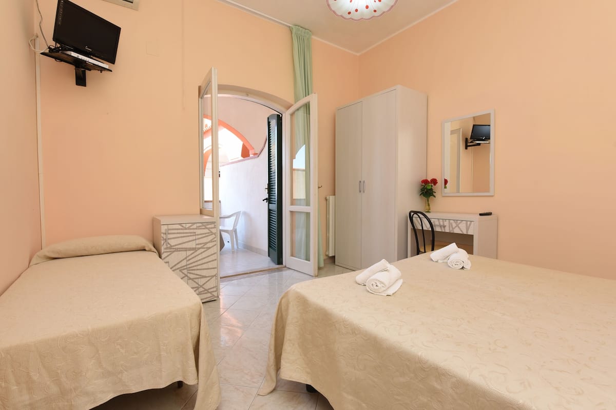 A hotel room with two beds, a desk, a chair, a wardrobe, and a television.