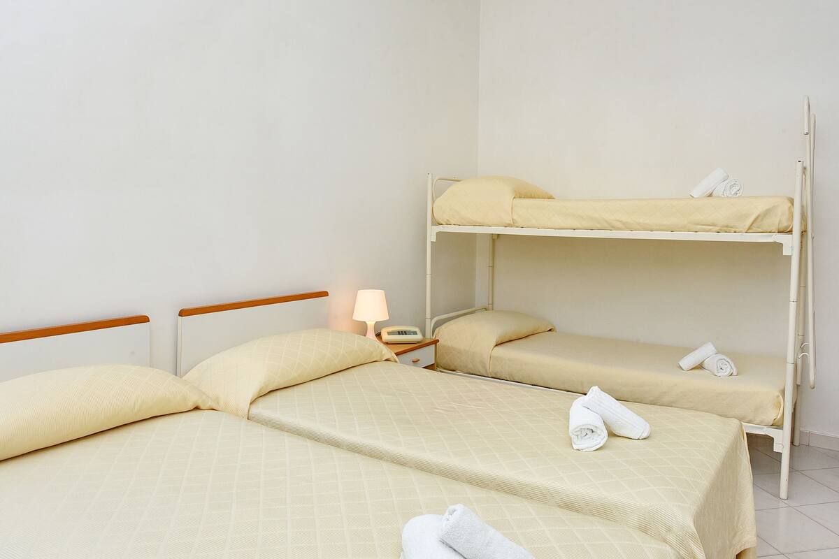 A room with two single beds and a bunk bed, each with neatly made beds and towels.
