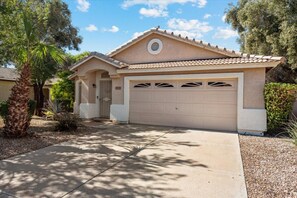 A single-story house with a beige facade, a tiled roof, and a garage with three doors. - Lovely home in a quiet neighborhood with private pool! (Peoria)