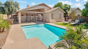A residential property with a swimming pool, a covered patio, and a fenced backyard.
