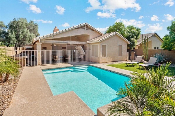 A residential property with a swimming pool, a covered patio, and a fenced backyard.