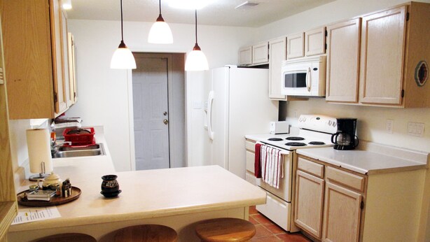 A kitchen with a central island, wooden stools, a microwave, a stove, and a refrigerator. - Relaxing/cozy home near Petroglyphs (Albuquerque)