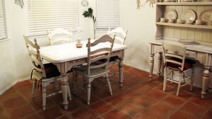 A dining area with a white table, four chairs, a chandelier, and a wall-mounted shelf with plates and cups. - Relaxing/cozy home near Petroglyphs (Albuquerque)
