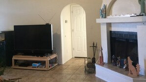 A living room with a television on a stand, a fireplace with decorative items, and a door in the background. - Relaxing/cozy home near Petroglyphs (Albuquerque)