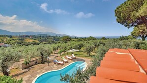 A swimming pool with lounge chairs, surrounded by greenery and a view of distant mountains.