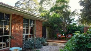 A brick house with large windows and a garden area with a patio and two red chairs. - Cowes Chapel Beach House (Cowes)