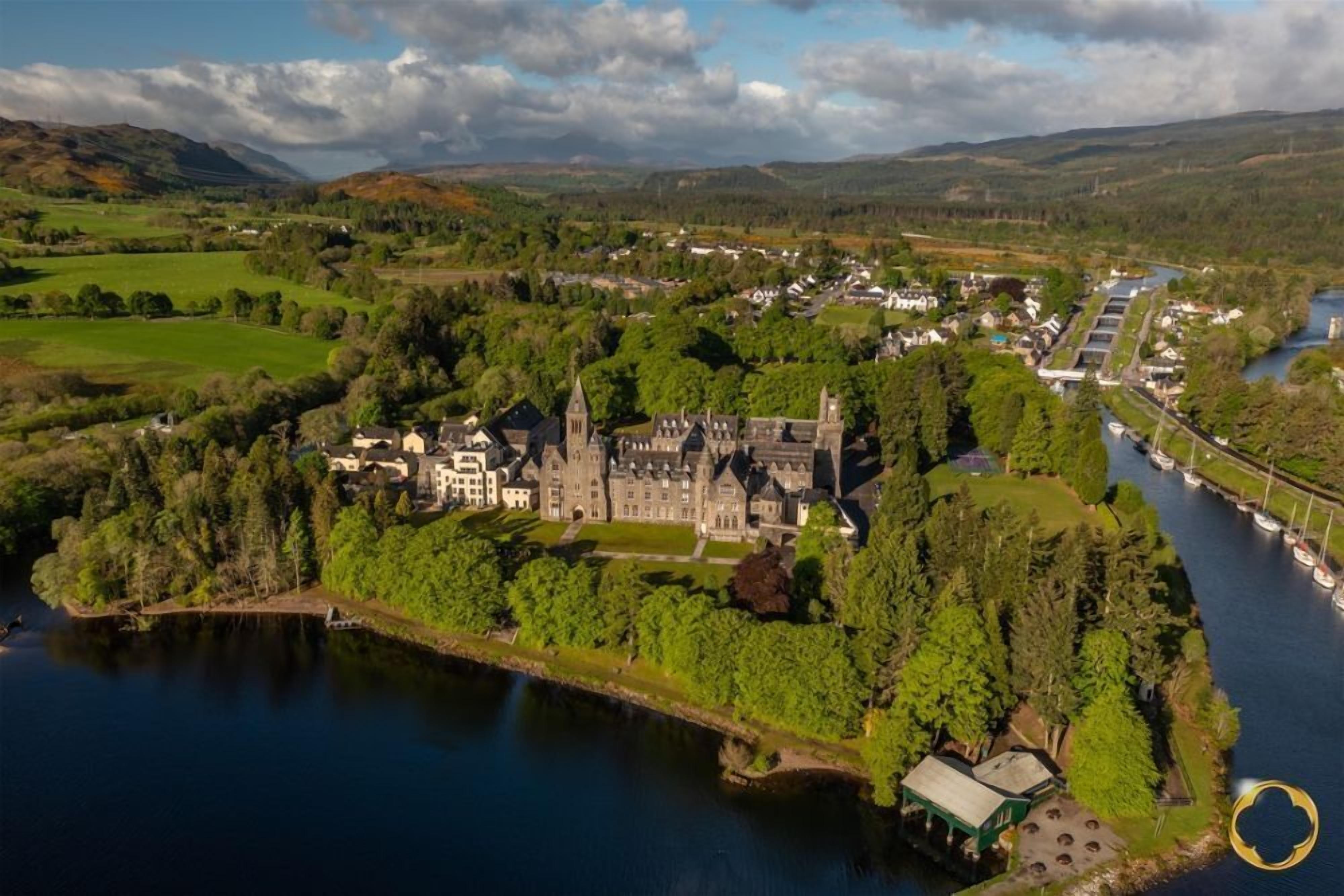 An aerial view of a castle surrounded by a lake, with a river and boats nearby.