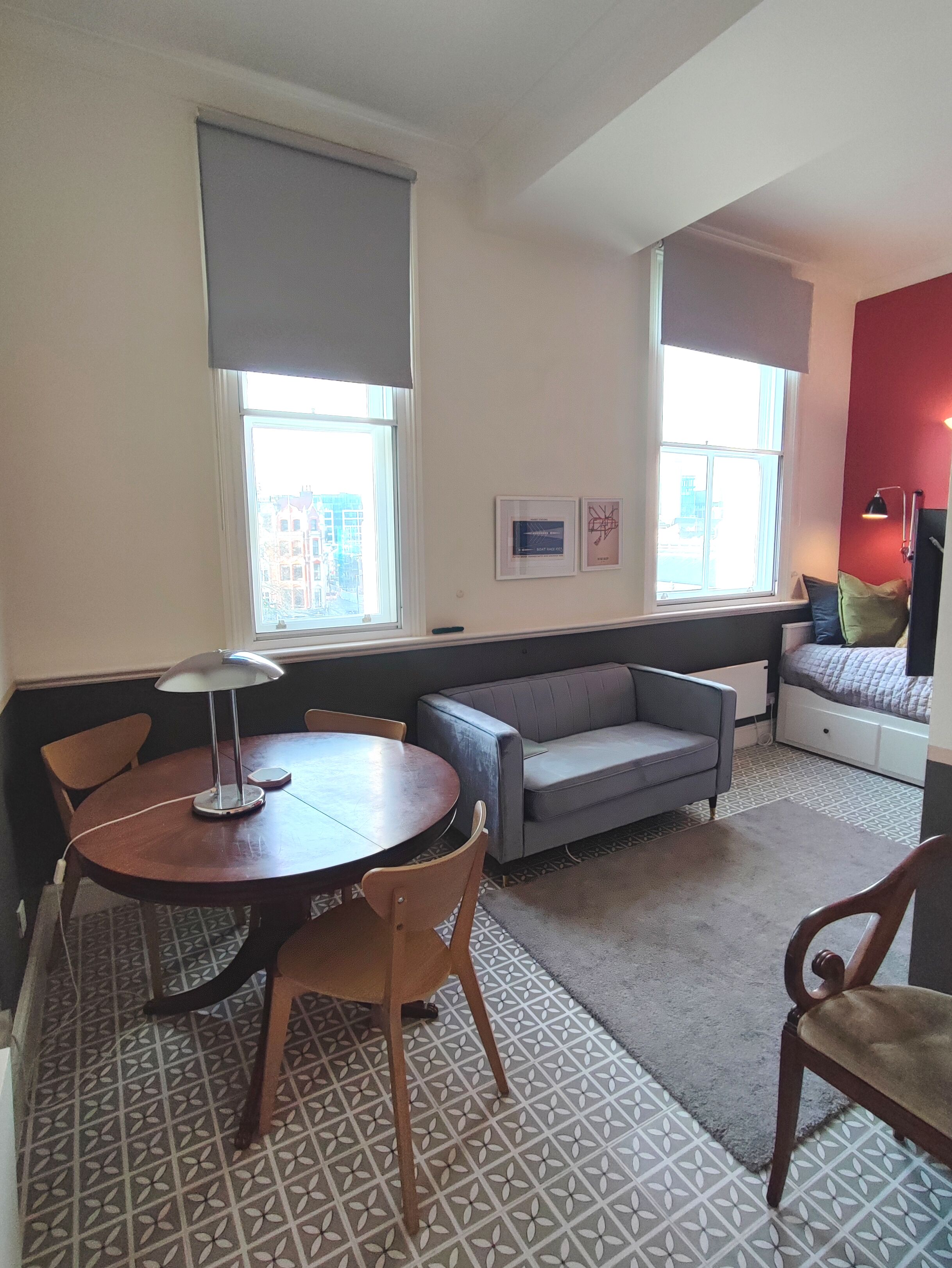 Una sala de estar con una mesa redonda, dos sillas, un sofá gris y una ventana con persianas.