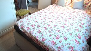 Ett sovrum med ett blommigt sängöverkast, en sänglampa och en stol.