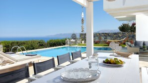 A poolside area with a table set for dining, a hammock, and a view of the sea. - Villa Greece Privat Seaview Villa with private heatable Pool  (Hersonissos)