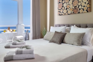 Ein Hotelzimmer mit Bett, Kissen, Meerblick, einem Tisch mit einem Getränk und einem Bild an der Wand.