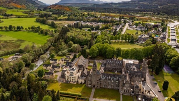 An aerial view of a historic estate with multiple buildings, including a large manor house, surrounded by lush green fields and trees. - Luxury self catering cottage with swimming pool  in the grounds of a Monastery on Loch Ness (Fort Augustus)