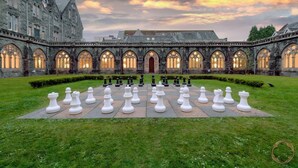 A courtyard with a chessboard arrangement of chess pieces in front of a historic building with arched windows and stone architecture. - Luxury self catering cottage with swimming pool  in the grounds of a Monastery on Loch Ness (Fort Augustus)