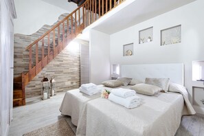 Un dormitorio con una escalera de madera, una cama grande con muchos cojines y un cabecero con luces fijadas a la pared.