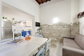 Una cocina moderna con protector mural de piedra, una mesa de comedor con sillas, un sofá y un televisor montado en la pared.