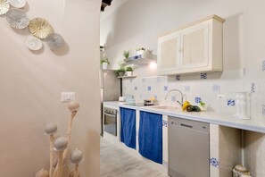 Una cocina con armarios blancos, baldosas azules y blancas estampadas, un lavavajillas y una encimera con distintos objetos.
