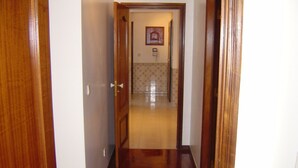 Un pasillo de madera que conduce a una habitación con piso de baldosas y un cuadro en la pared.
